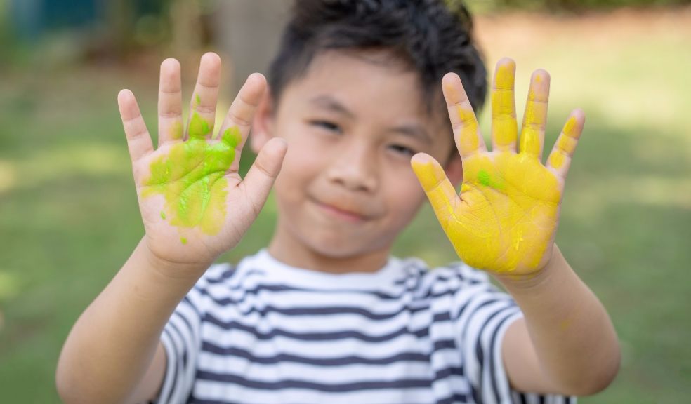 Happy funny child draws laughing shows hands dirty with paint. Family.