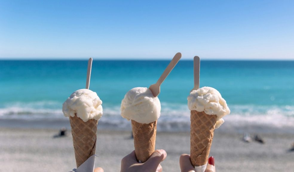 Three ice cream  cones being held up near the beach