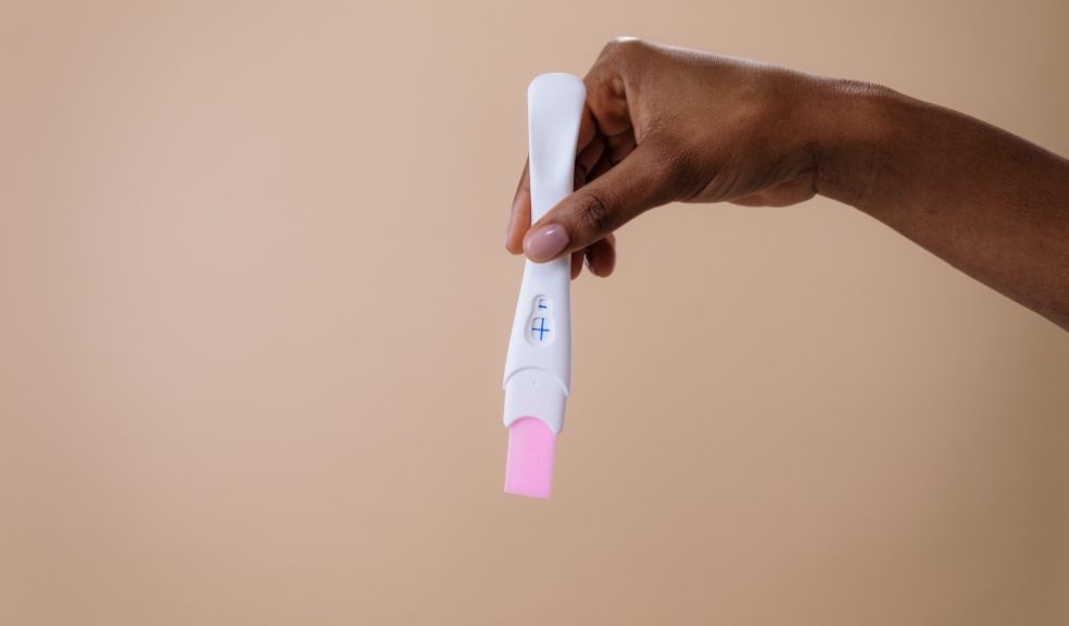 A woman's hand holding a positive pregnancy test on a neutral background