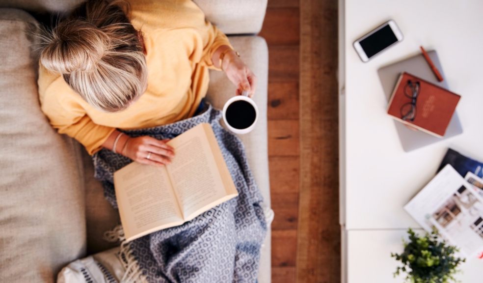 Woman reading book on sofa with a cup of coffee. Getty Images/iStockphoto