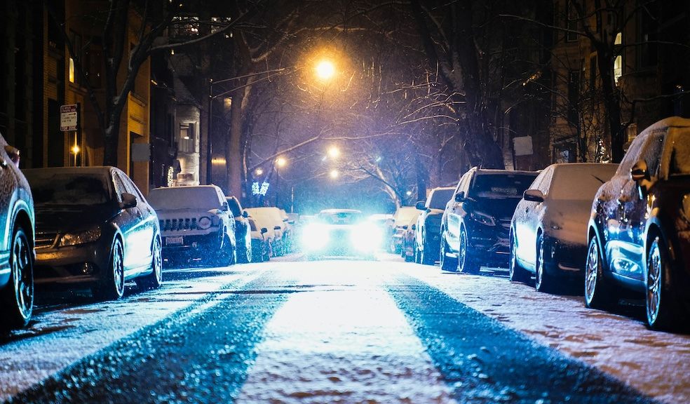 Snow settling on the road with cars parked either side