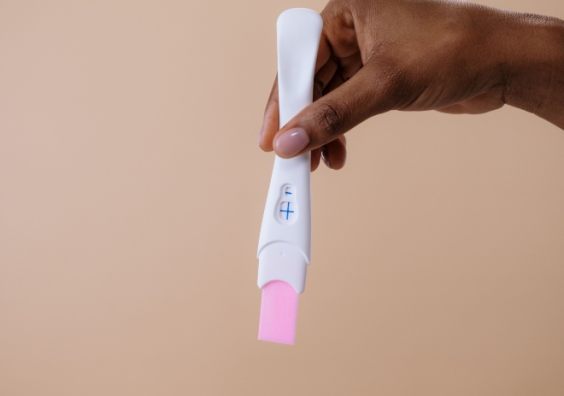 A woman's hand holding a positive pregnancy test on a neutral background