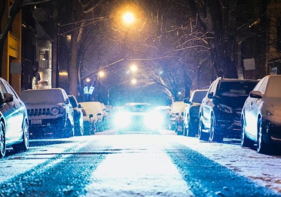 Snow settling on the road with cars parked either side