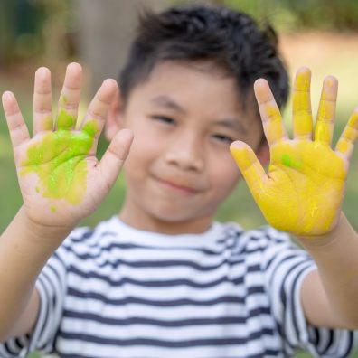 Happy funny child draws laughing shows hands dirty with paint. Family.