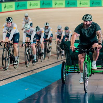 A man on a trike watches cyclists in a velodrome 