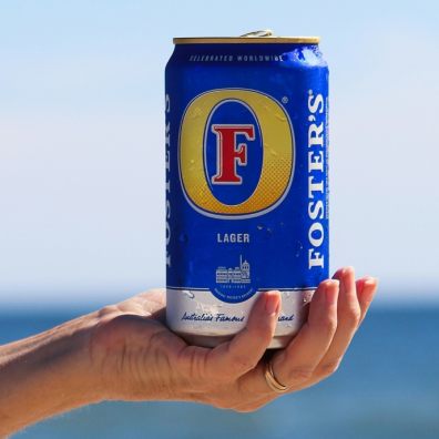 A can of beer being held in front of a beach