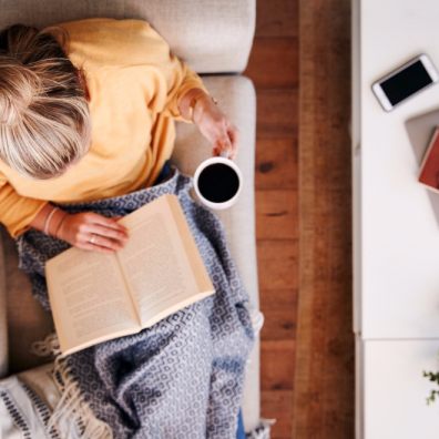 Woman reading book on sofa with a cup of coffee. Getty Images/iStockphoto