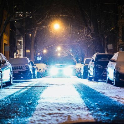 Snow settling on the road with cars parked either side